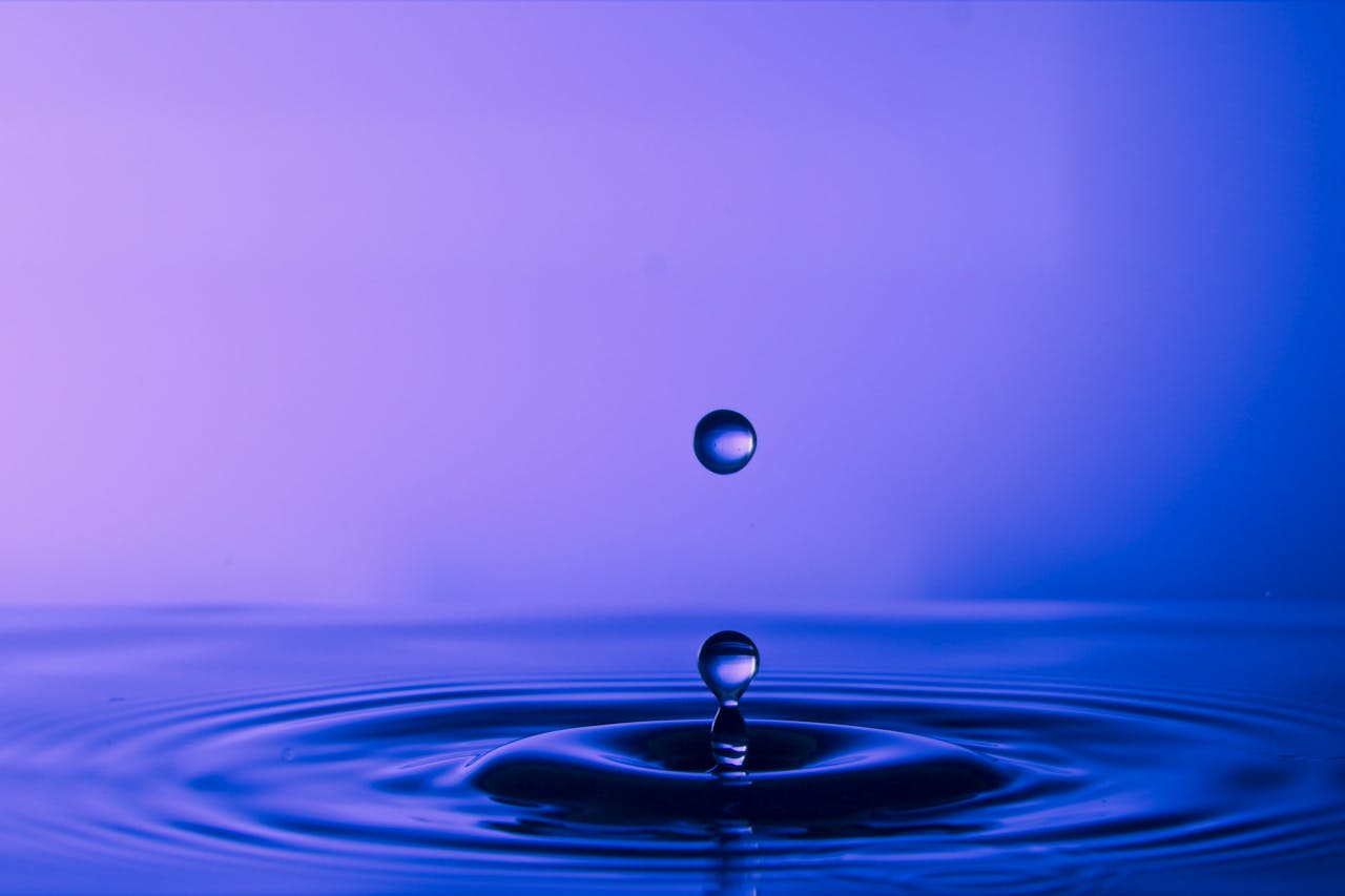 A mesmerizing blue water droplet captured mid-air, focusing on its reflection and ripple effect.